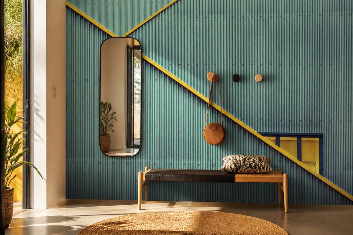 Contemporary hallway with bench and sculptural mirror transformed by bold blue wallpaper with sharp yellow architectural lines.